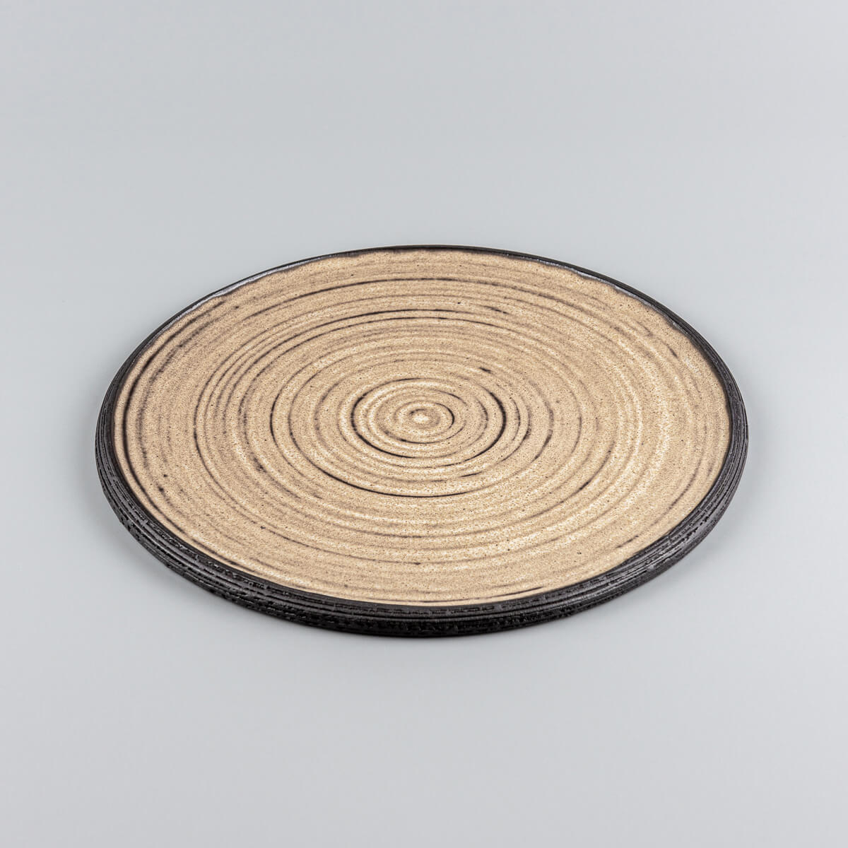 Close-up of textured handmade ceramic plate with carved concentric rings and unglazed black rim.