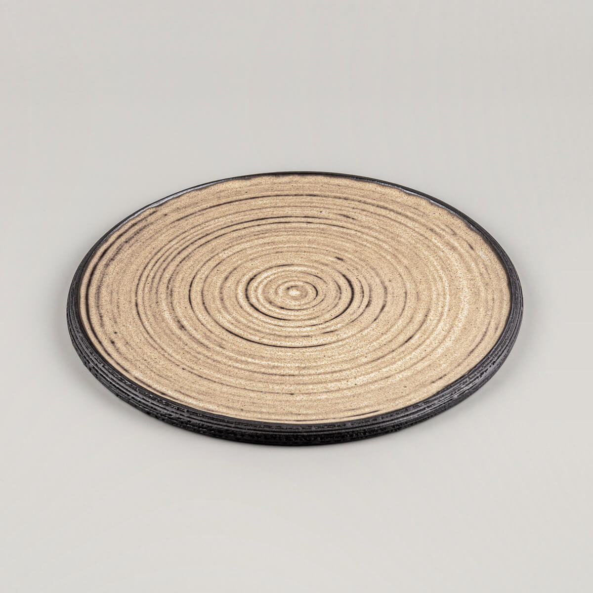 Close-up of textured handmade ceramic plate with carved concentric rings and unglazed black rim.