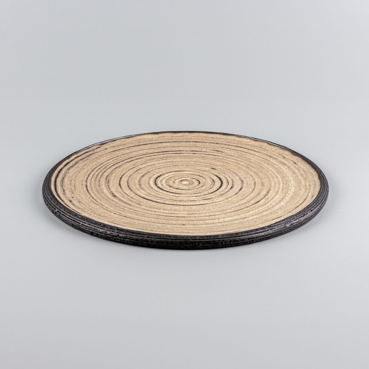 Handmade ceramic plate with concentric circle texture in matte ocher glaze and black clay rim.