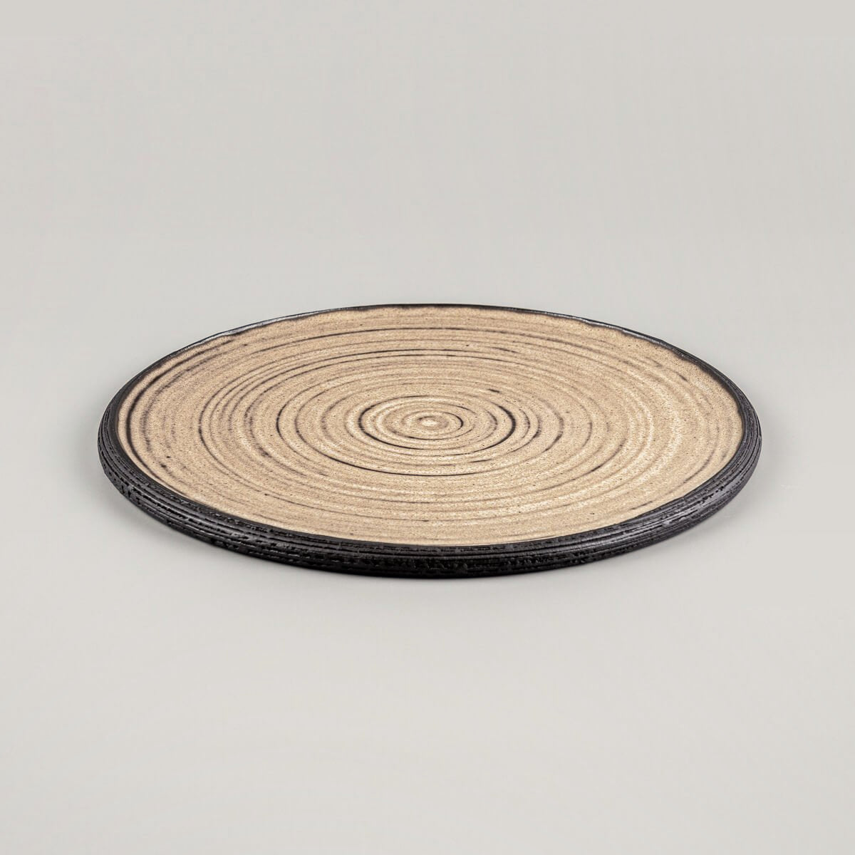 Handmade ceramic plate with concentric circle texture in matte ocher glaze and black clay rim.