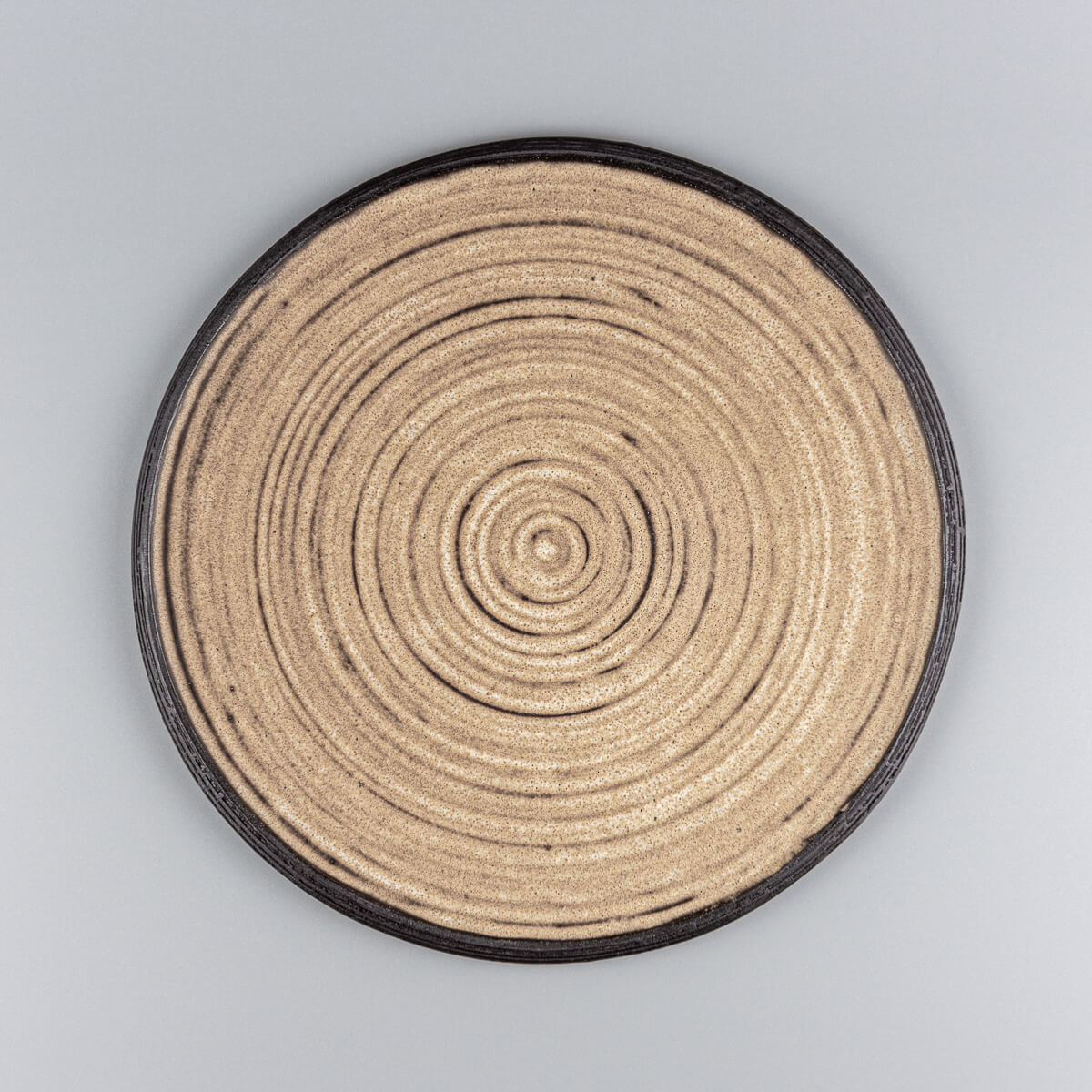 Handmade ceramic plate with matte ocher glaze and carved black rim for fine dining presentation.