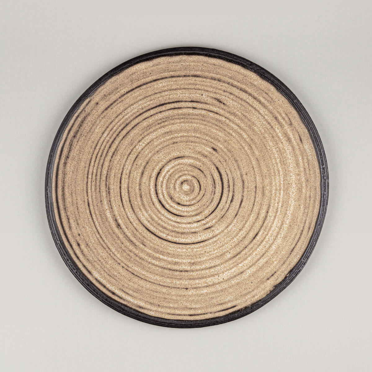 Handmade ceramic plate with matte ocher glaze and carved black rim for fine dining presentation.