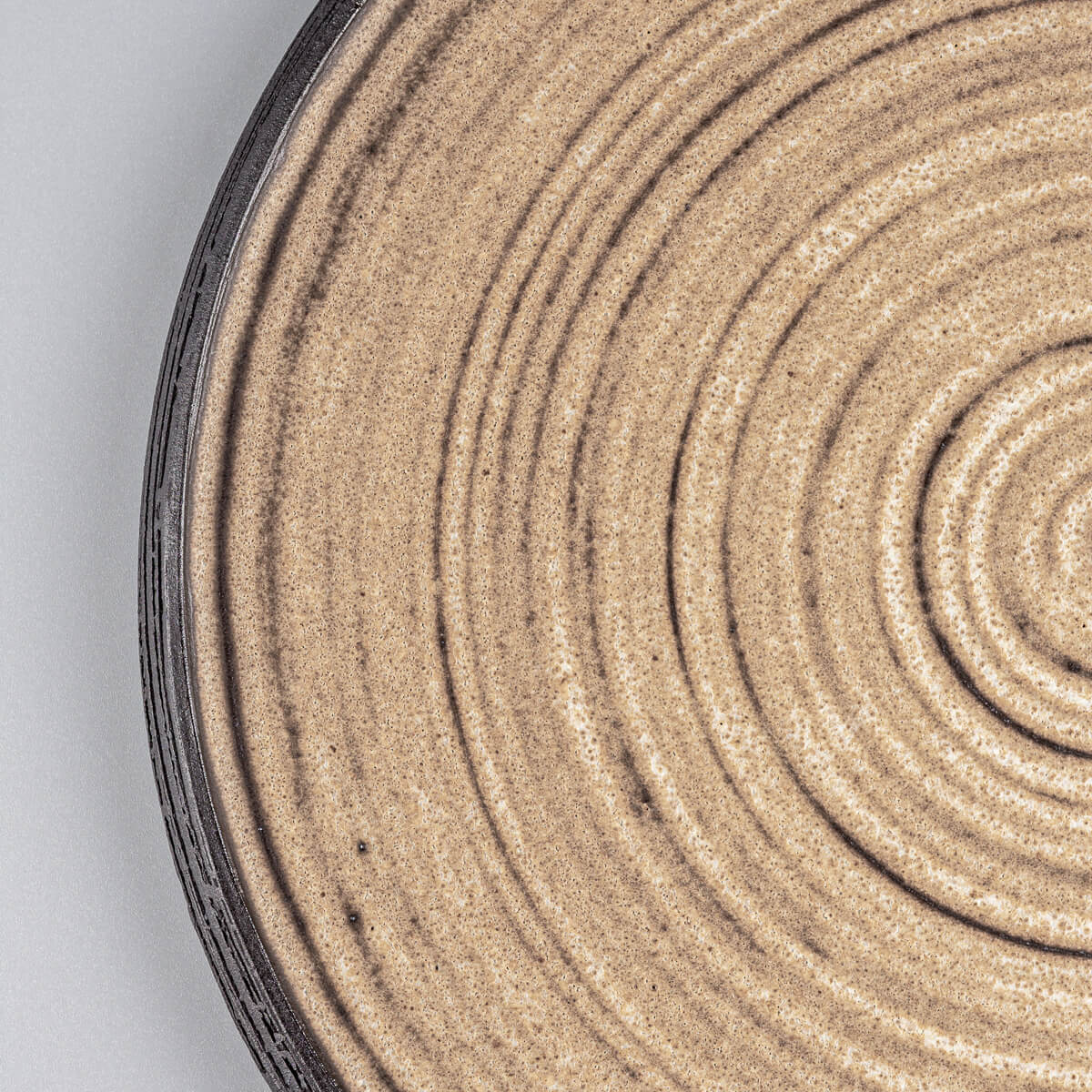 Close-up of textured handmade ceramic plate with carved rim in black stoneware.