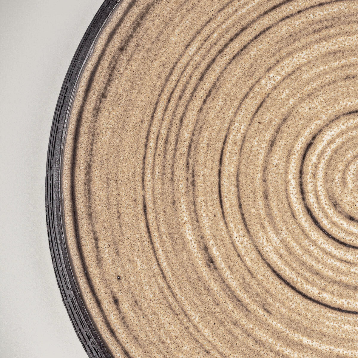 Close-up of textured handmade ceramic plate with carved rim in black stoneware.