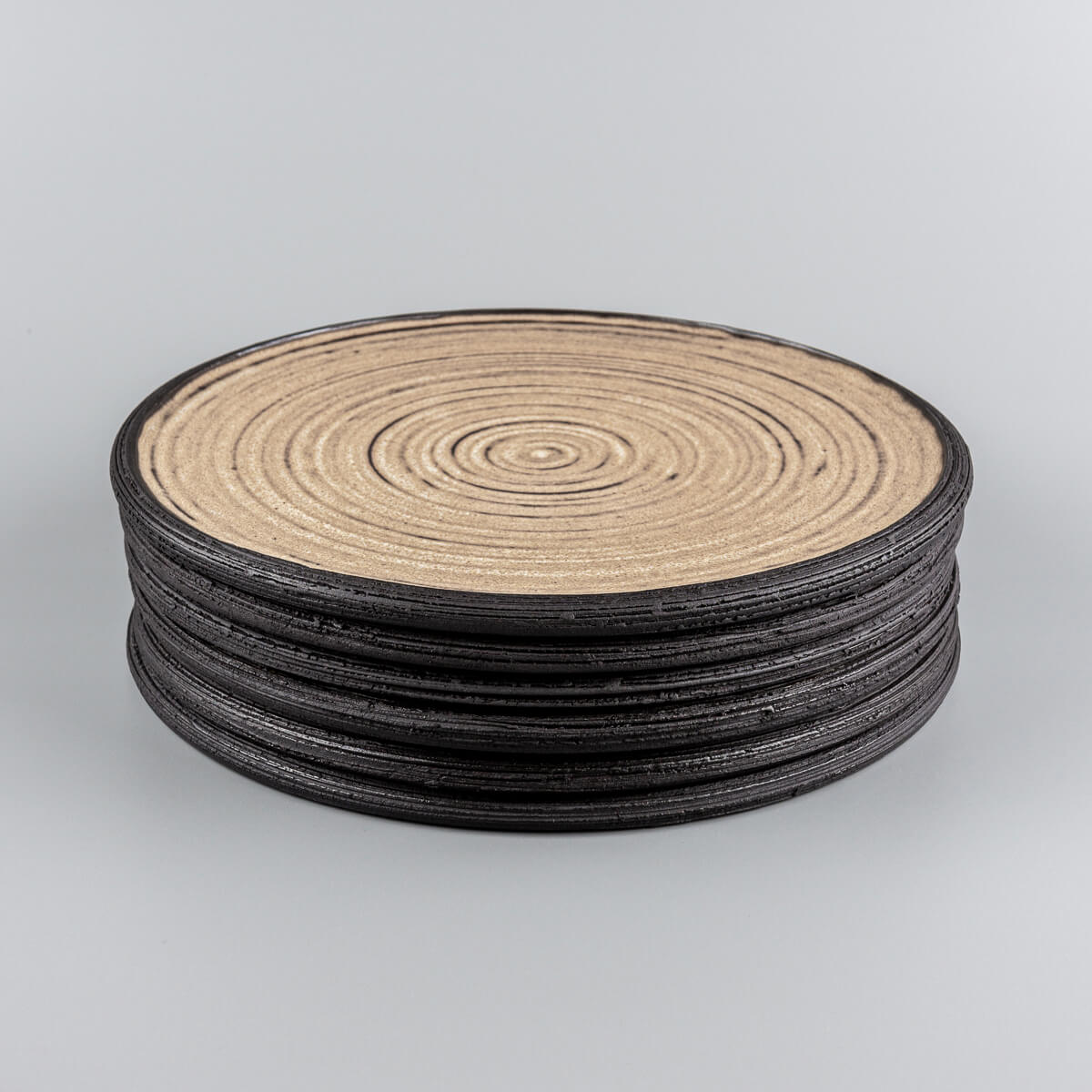 Stacked handmade ceramic plates with matte ocher glaze and carved rims.