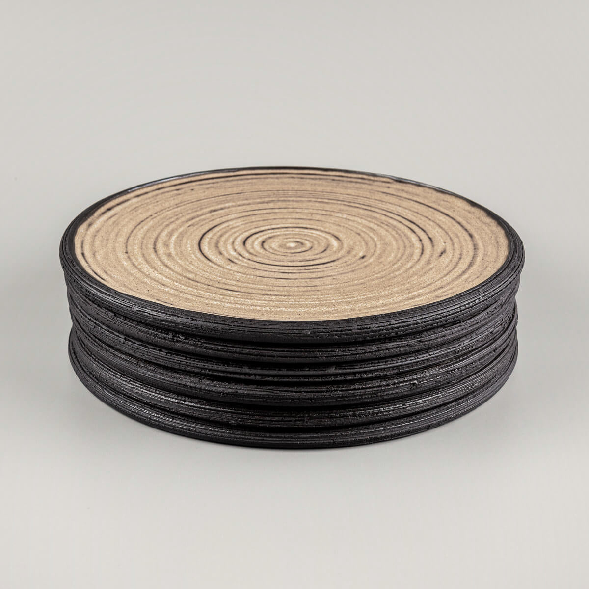 Stacked handmade ceramic plates with matte ocher glaze and carved rims.