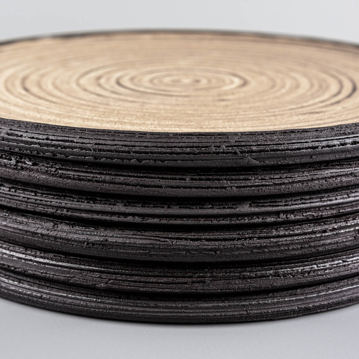 Side view of handmade ceramic plates with textured rims in black stoneware.