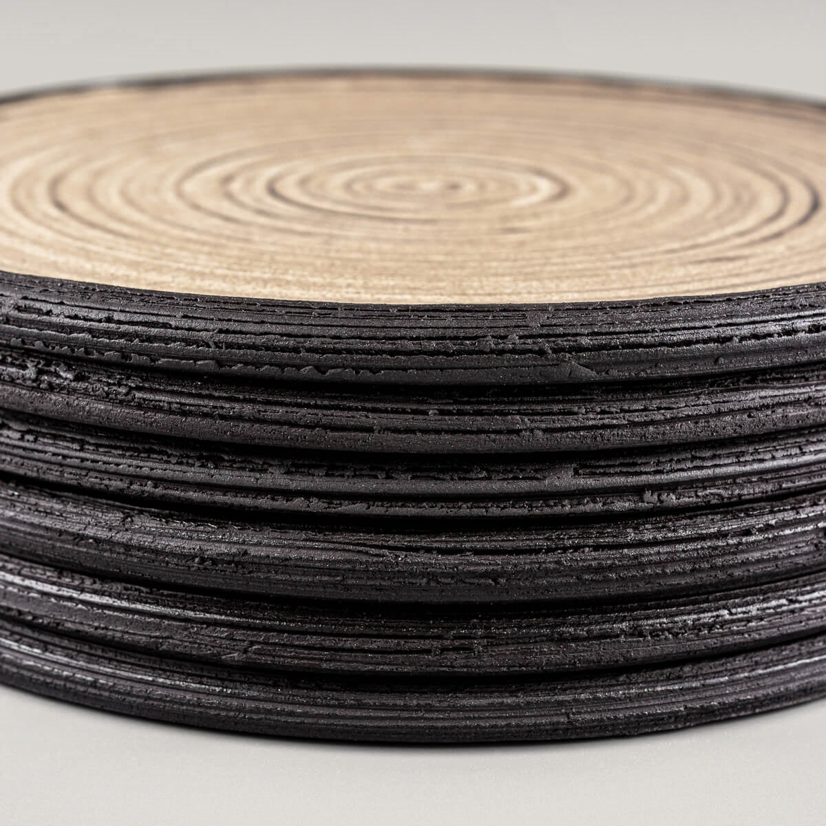 Side view of handmade ceramic plates with textured rims in black stoneware.