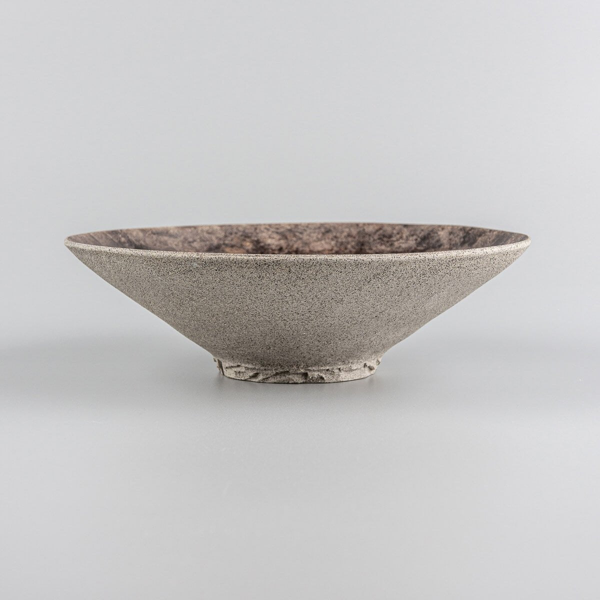 Handcrafted stoneware plate with textured base and earthy-toned glazed surface.