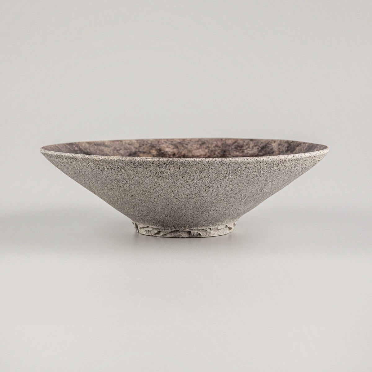 Handcrafted stoneware plate with textured base and earthy-toned glazed surface.