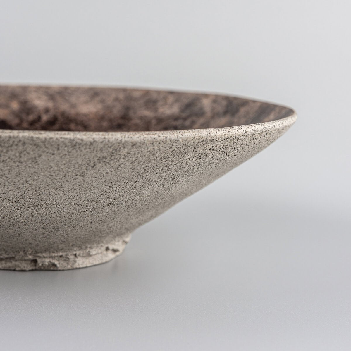 Side profile of handcrafted stoneware plate with cone-shaped design and unglazed exterior.