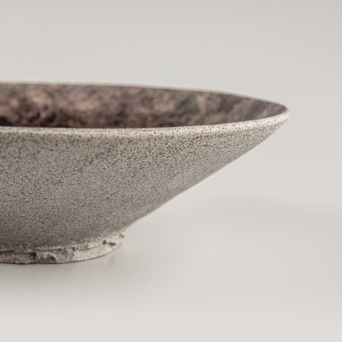 Side profile of handcrafted stoneware plate with cone-shaped design and unglazed exterior.