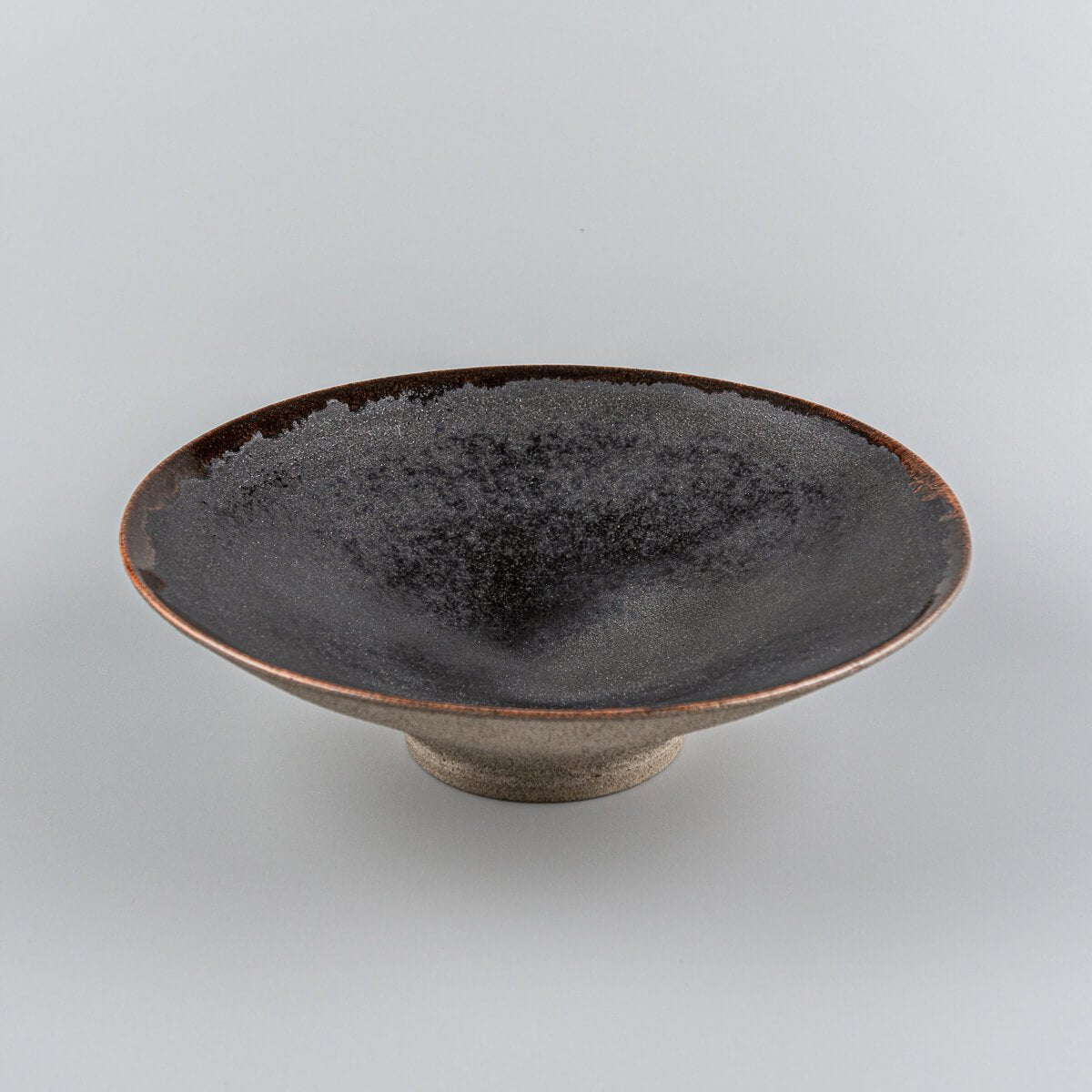 Handcrafted artisanal ceramic plate with elevated base, black matte glaze interior, and warm orange rim for fine dining.