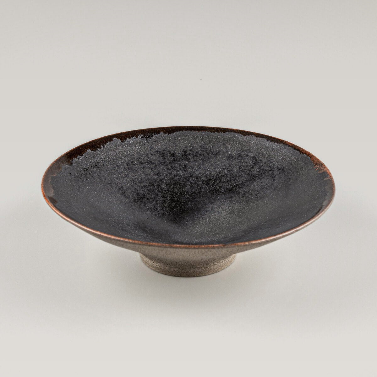 Handcrafted artisanal ceramic plate with elevated base, black matte glaze interior, and warm orange rim for fine dining.