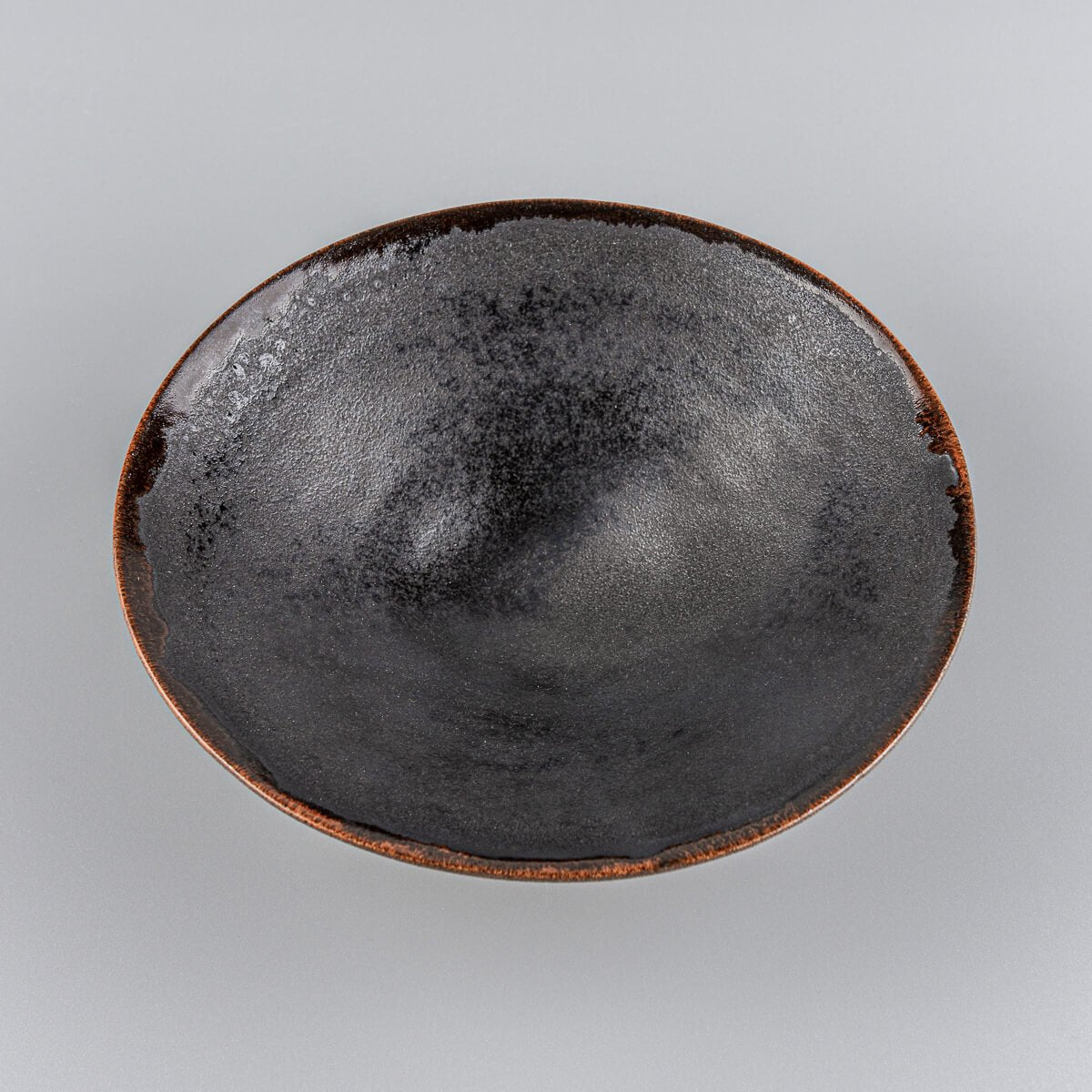 Top view of artisanal ceramic plate showing deep black glaze and orange-tinted edges.