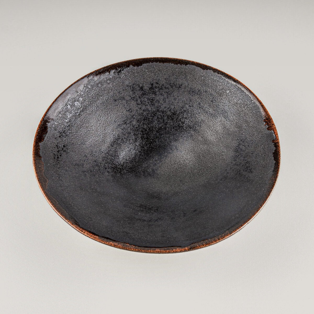 Top view of artisanal ceramic plate showing deep black glaze and orange-tinted edges.
