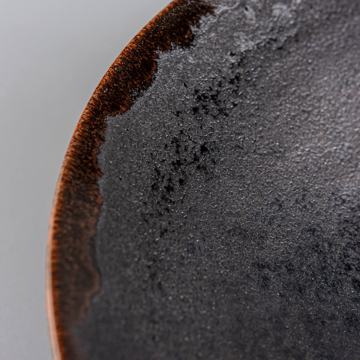 Detail of black matte glaze transitions into orange rim on artisanal dining plate.