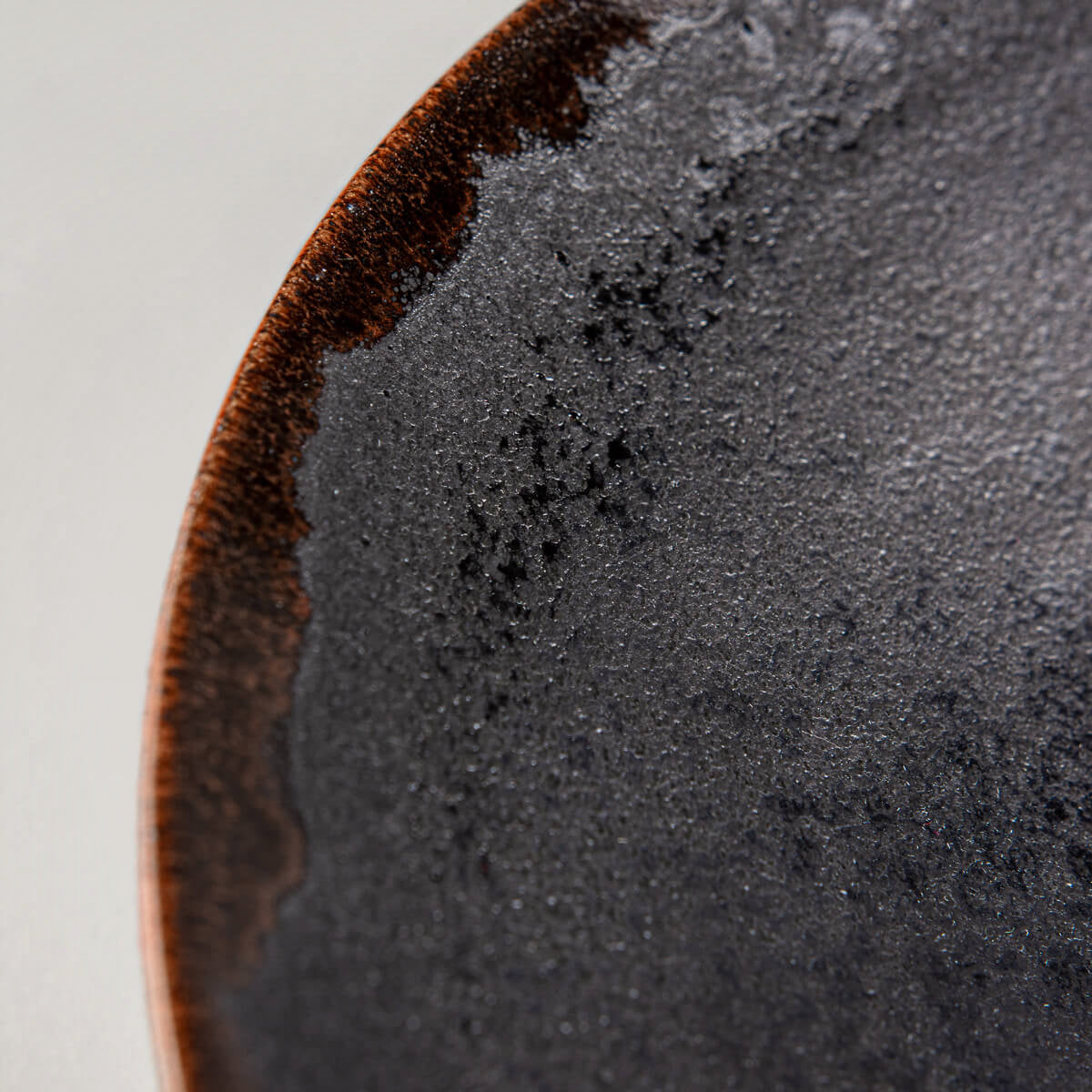 Detail of black matte glaze transitions into orange rim on artisanal dining plate.