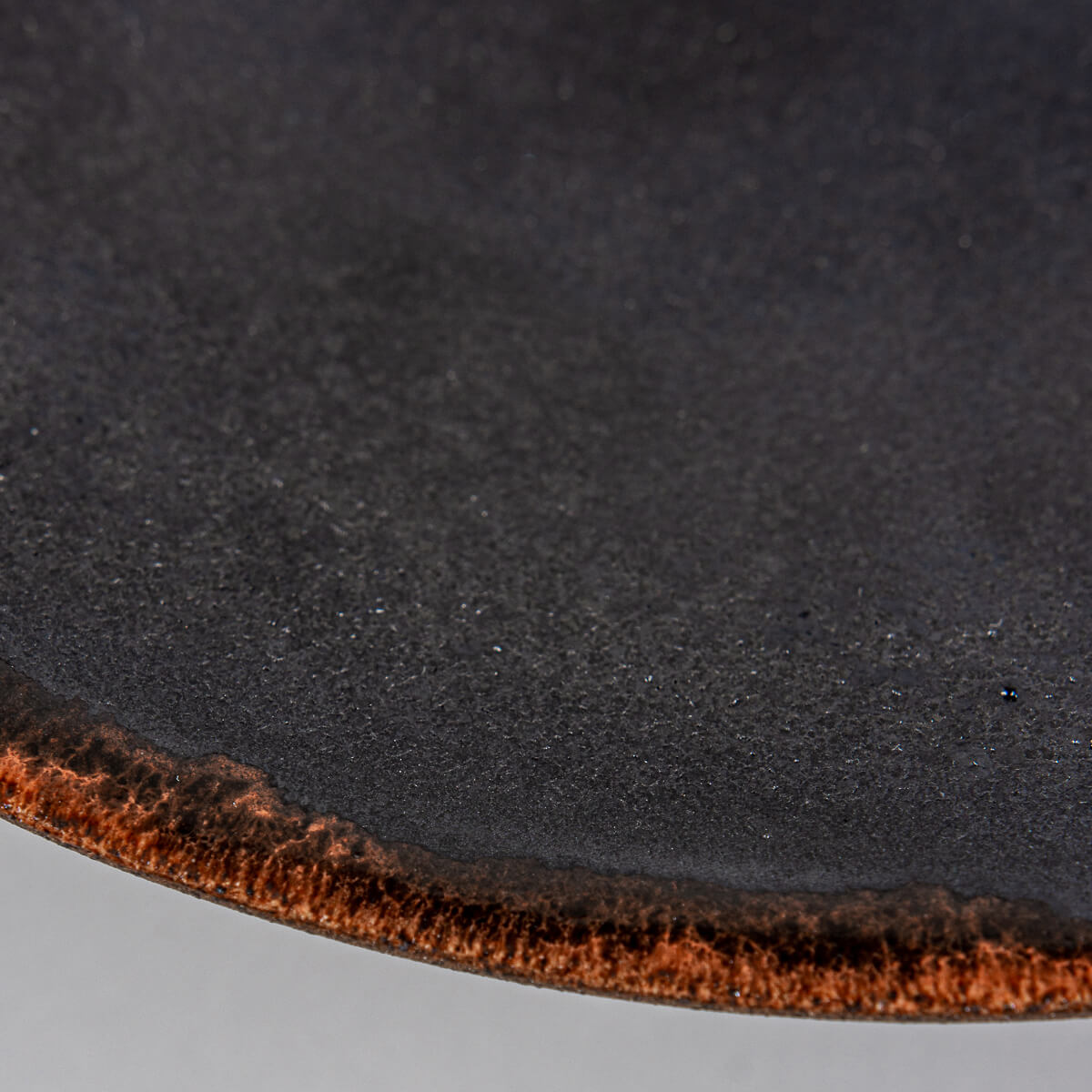 Close-up of artisanal ceramic plate rim showing smooth black glaze and semi-transparent orange accent for luxury tableware.