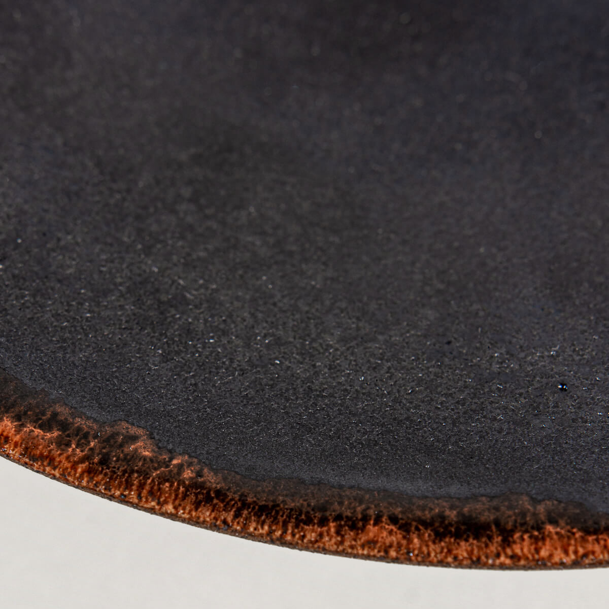 Close-up of artisanal ceramic plate rim showing smooth black glaze and semi-transparent orange accent for luxury tableware.