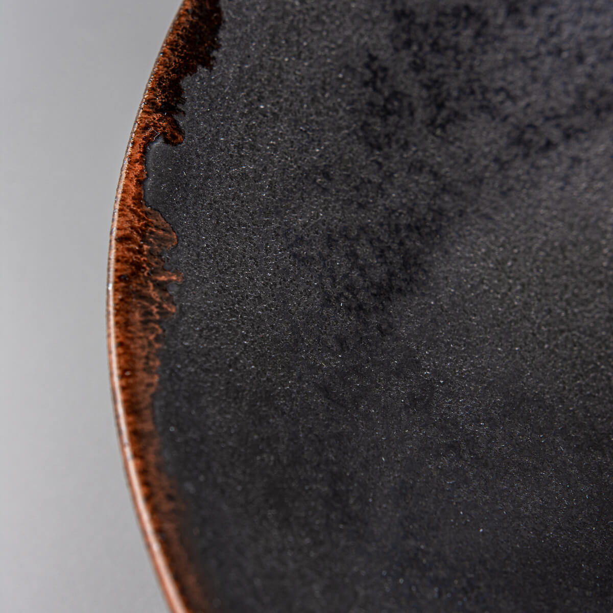 Edge detail of artisanal ceramic plate highlighting orange semi-transparent glaze.