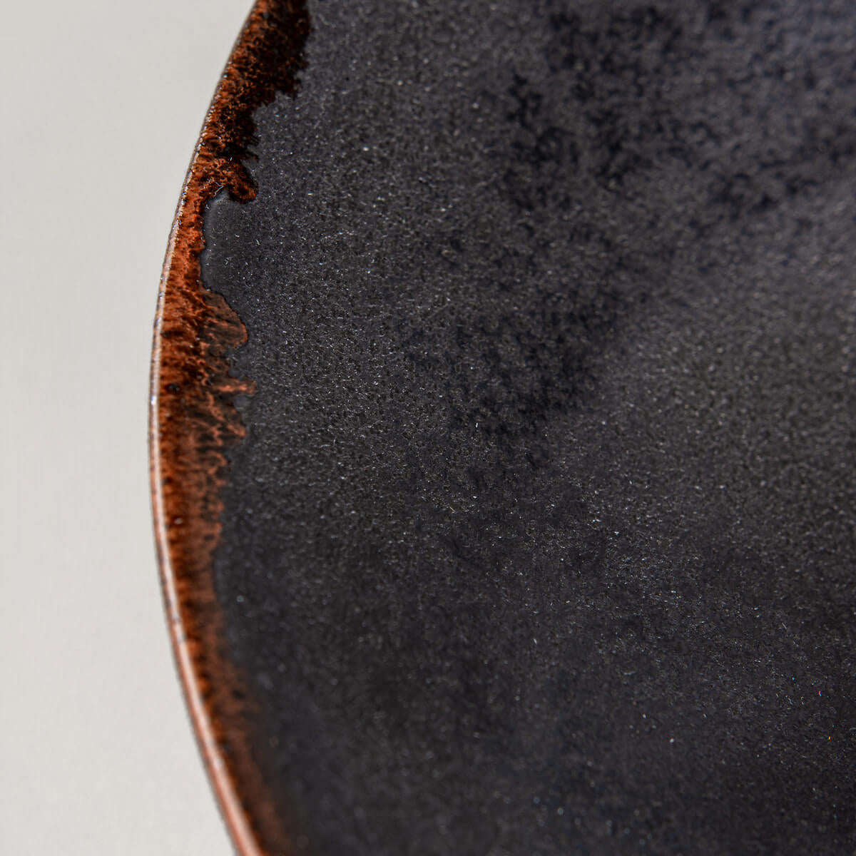 Edge detail of artisanal ceramic plate highlighting orange semi-transparent glaze.