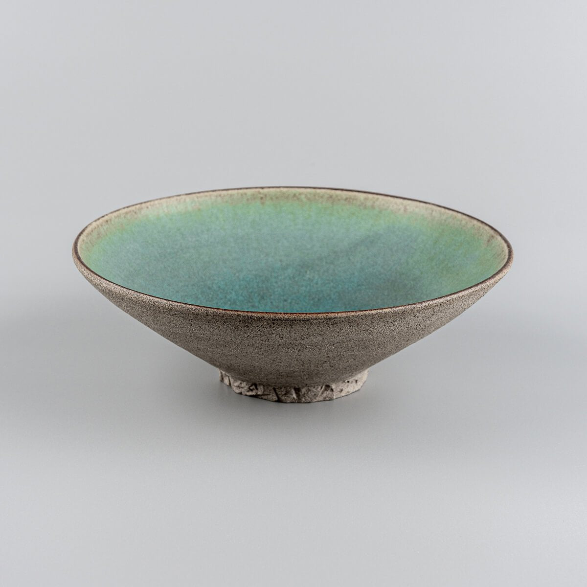Unique handmade ceramic plate showcasing turquoise interior and earthy clay exterior.