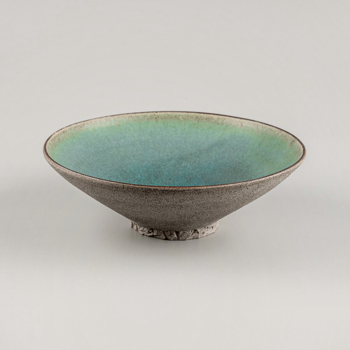 Unique handmade ceramic plate showcasing turquoise interior and earthy clay exterior.
