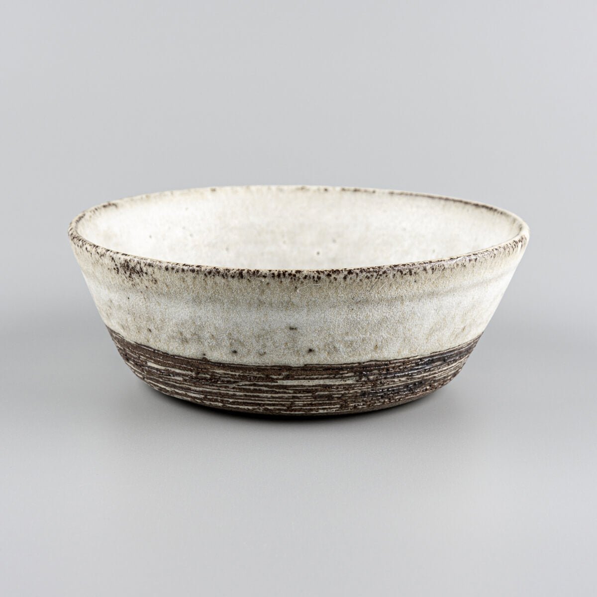 Handmade pottery bowl with matte white glaze and exposed carved stoneware texture.