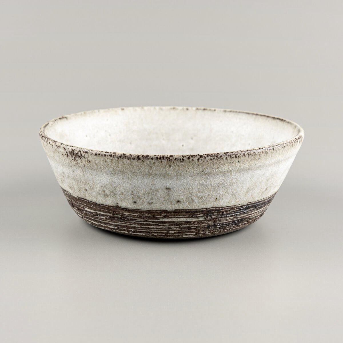 Handmade pottery bowl with matte white glaze and exposed carved stoneware texture.
