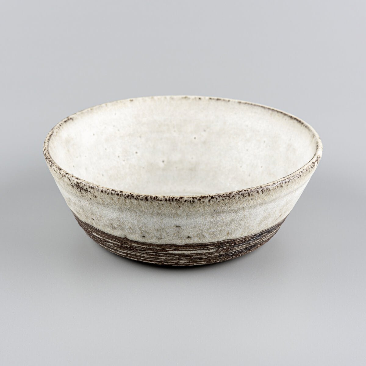 Side angle of artisanal stoneware bowl with carved horizontal lines and raw clay finish.