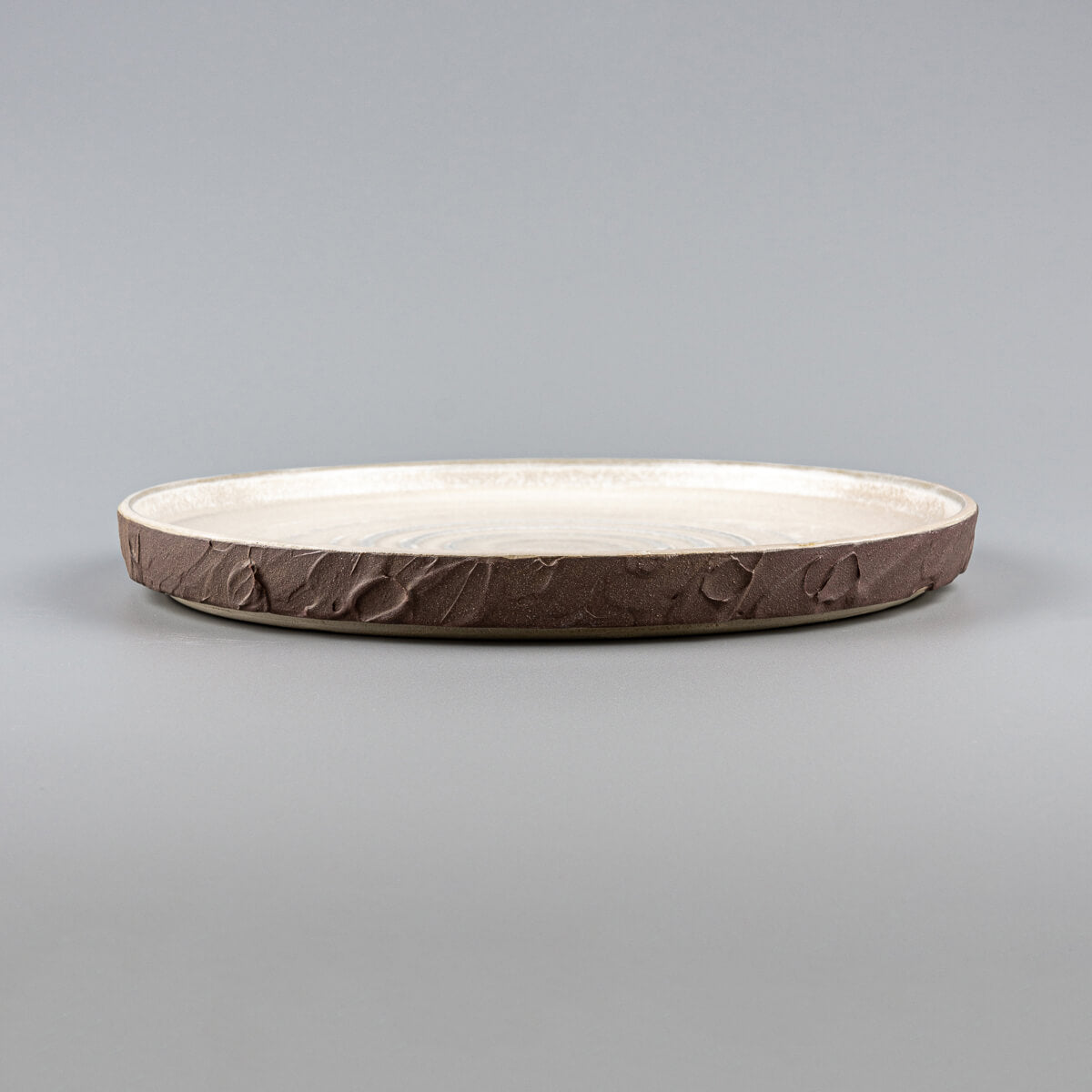 Elegant stoneware dinner plate with curved edges and textured spiral design for restaurant plating.