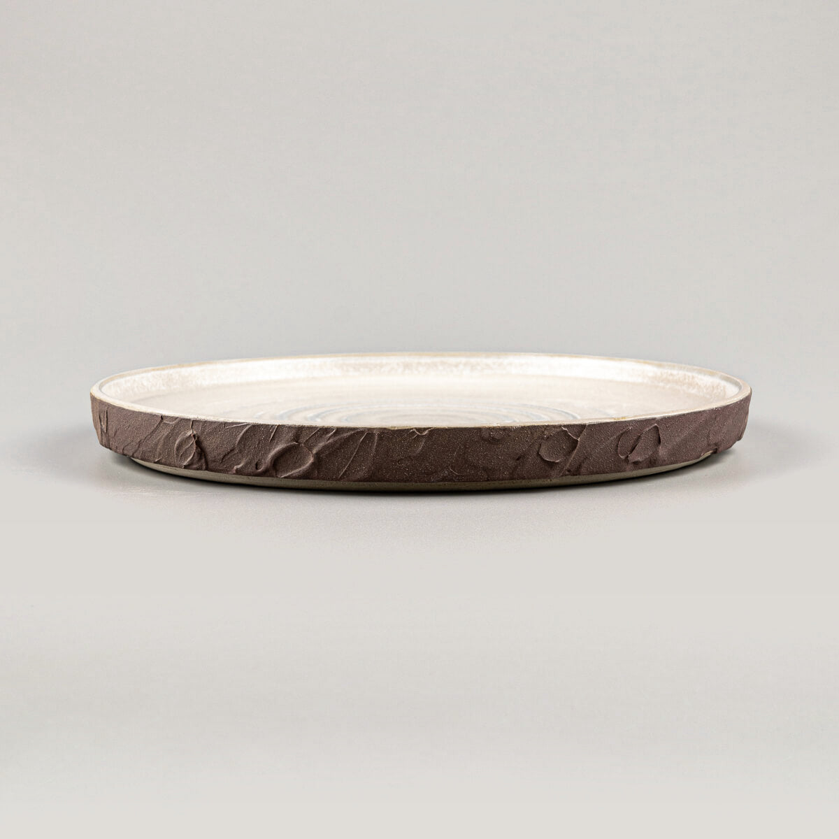 Elegant stoneware dinner plate with curved edges and textured spiral design for restaurant plating.