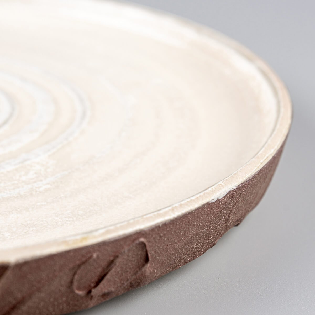 Side profile of handcrafted stoneware plate with spiral center and earthy exterior finish.