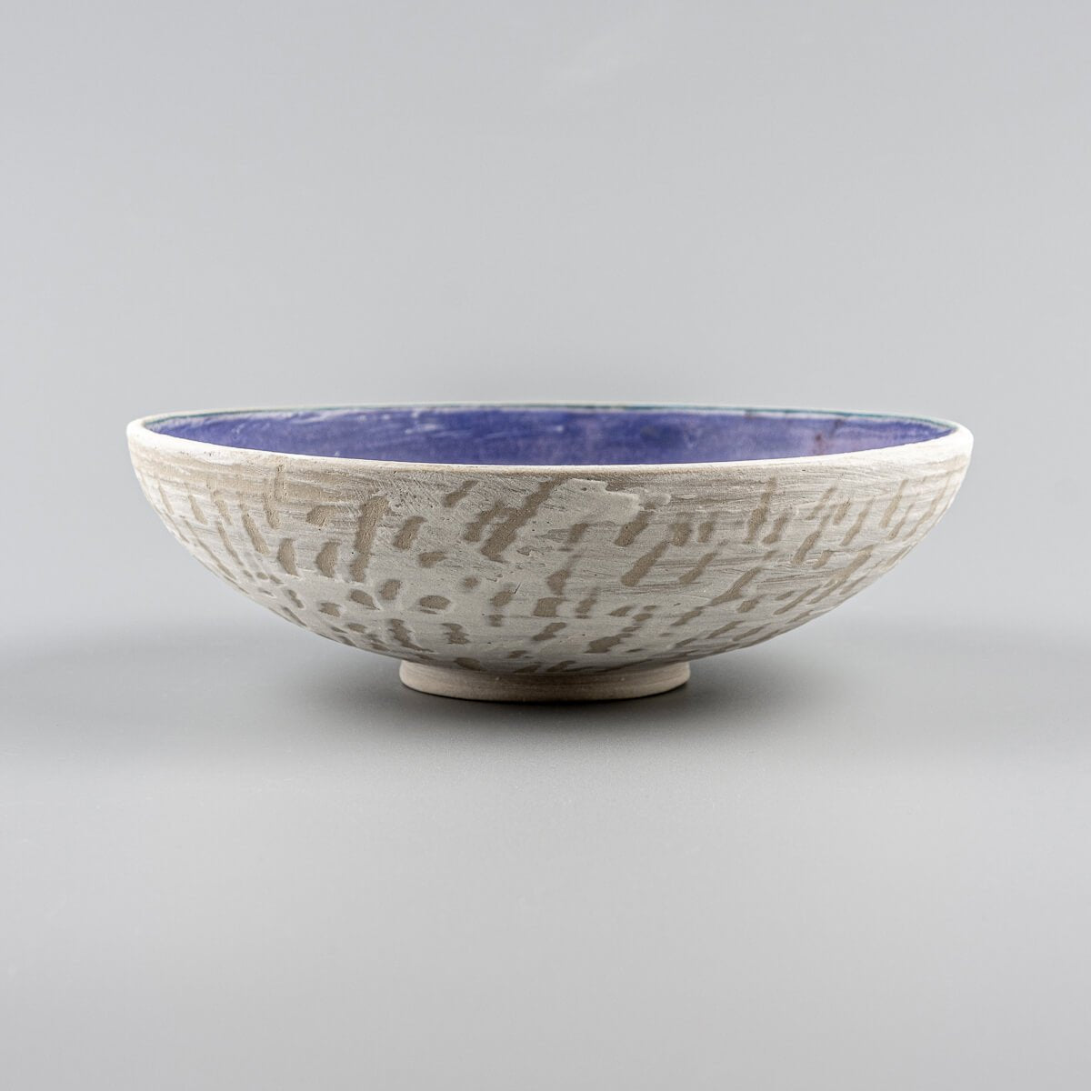 Side view of handmade pottery bowl with textured white exterior and amethyst glazed interior.