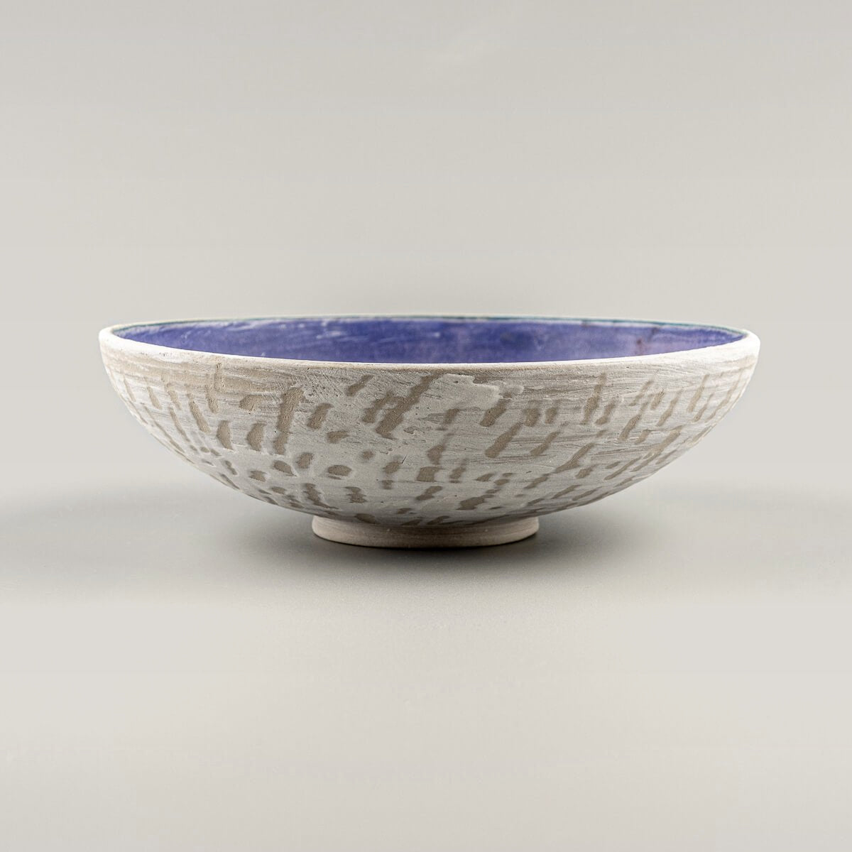 Side view of handmade pottery bowl with textured white exterior and amethyst glazed interior.