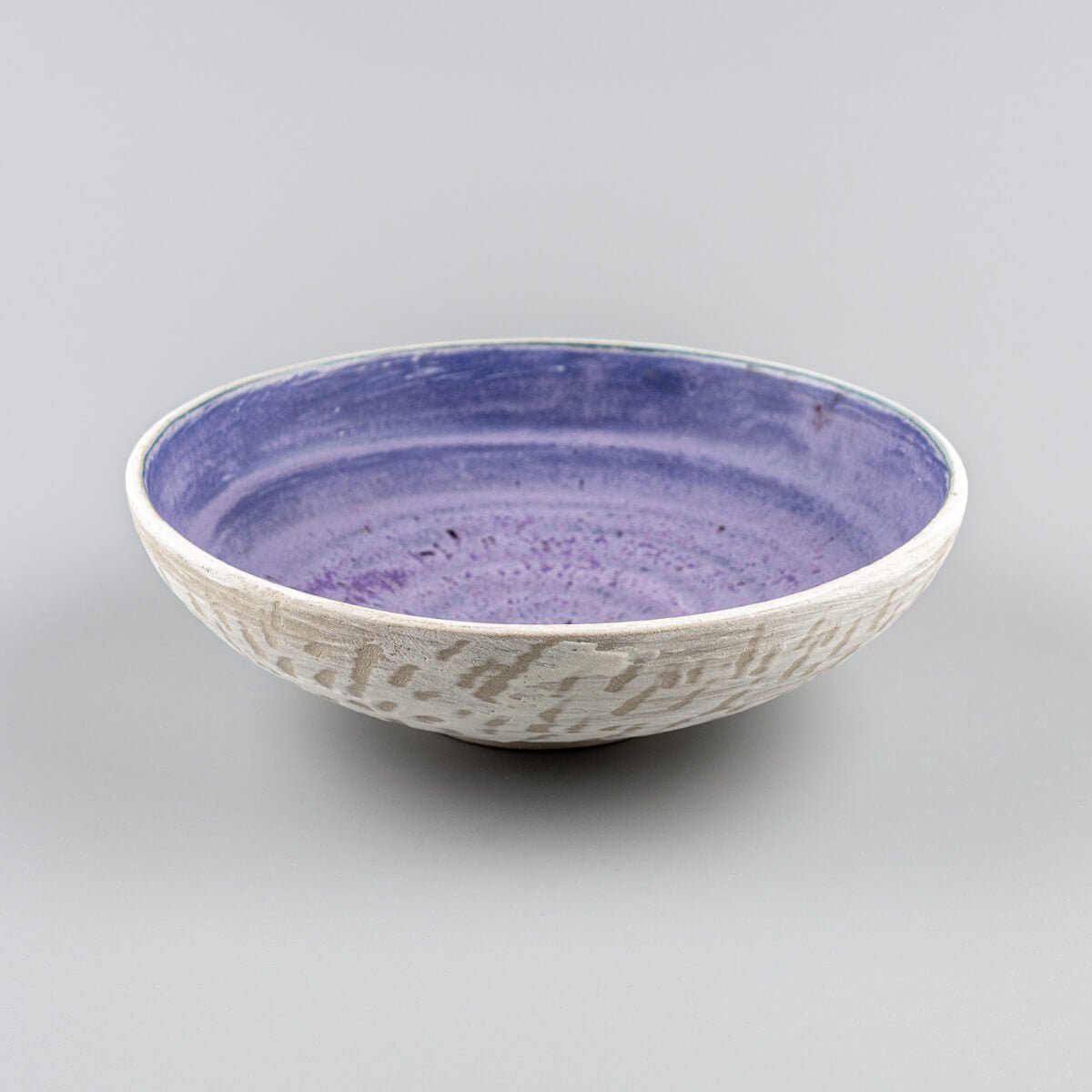 Profile shot of handmade pottery bowl on footed base with matte amethyst interior.