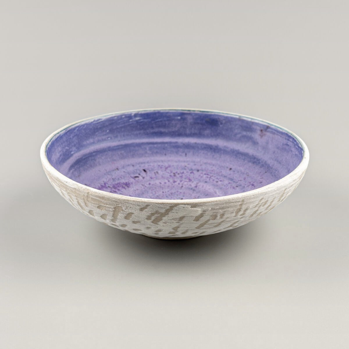 Profile shot of handmade pottery bowl on footed base with matte amethyst interior.