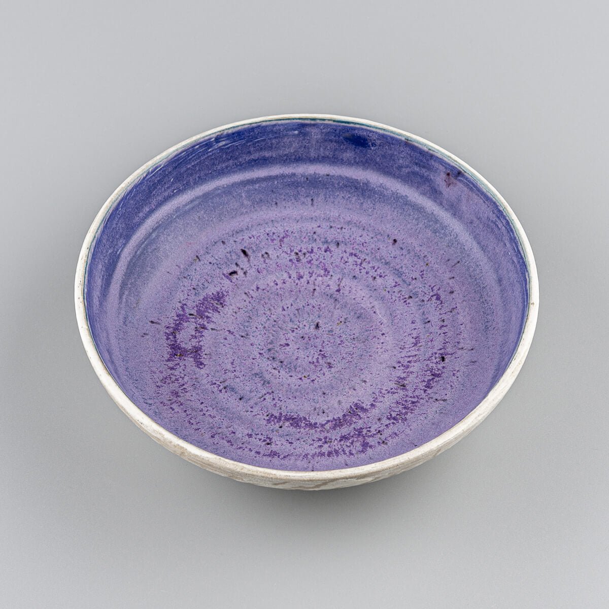 Angled view of handmade bowl with slip-decorated outer surface and vivid inner glaze.