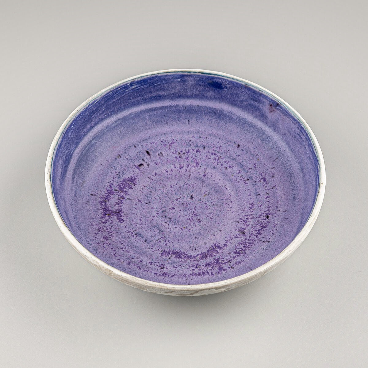 Angled view of handmade bowl with slip-decorated outer surface and vivid inner glaze.