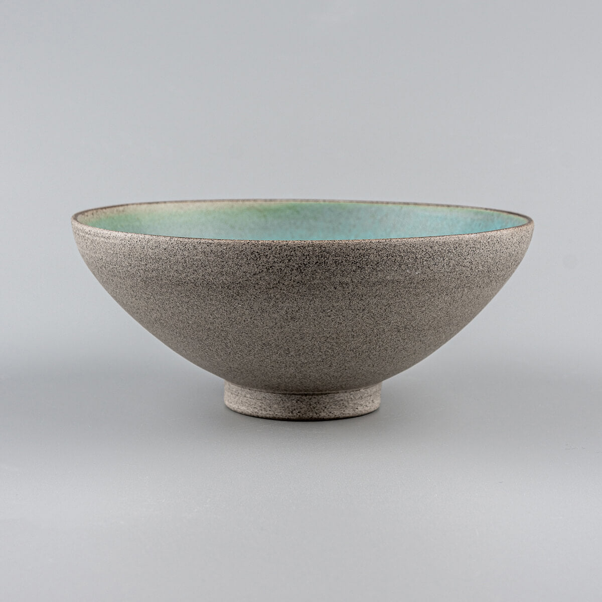 Side view of handmade ceramic bowl with raw stoneware exterior and turquoise glazed interior.