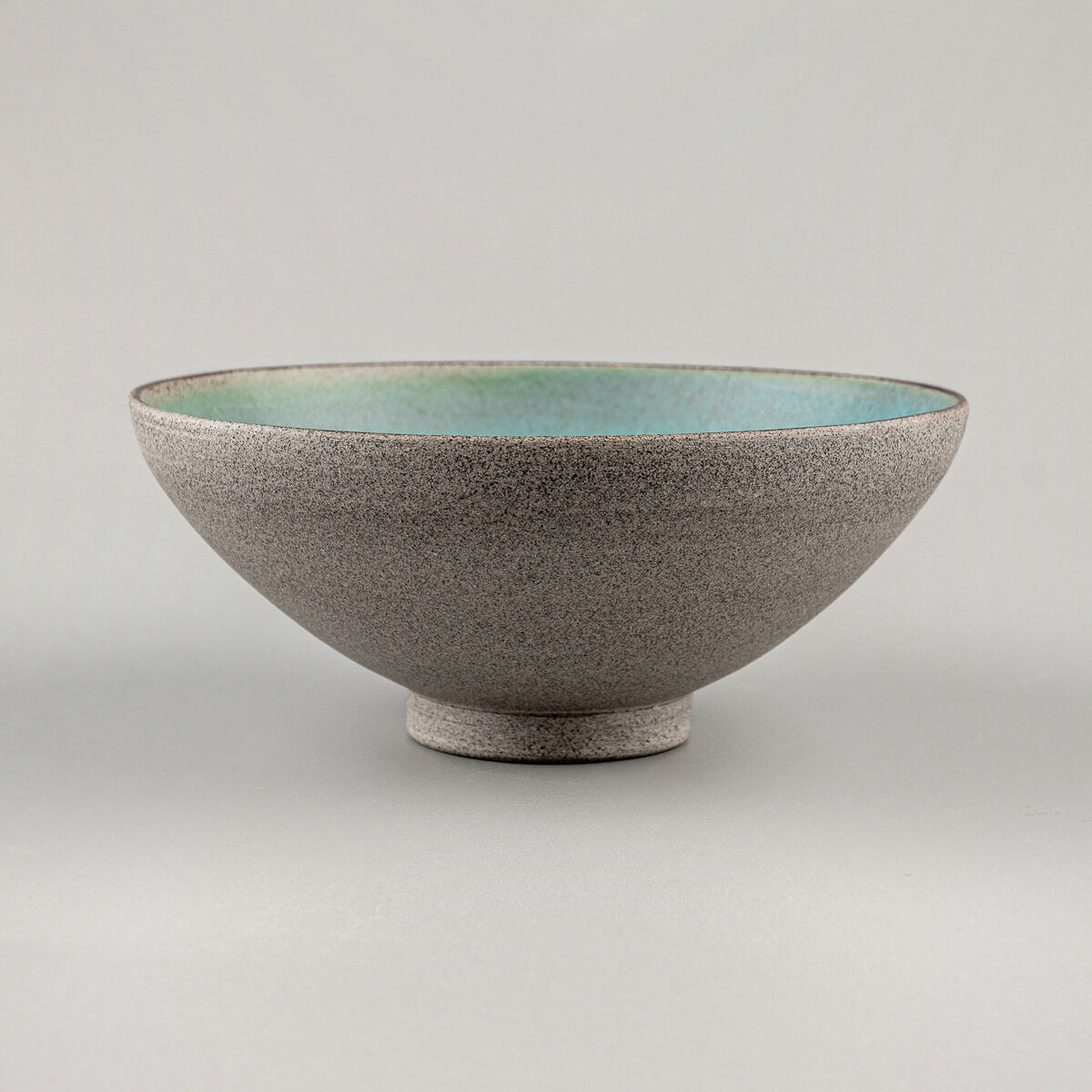 Side view of handmade ceramic bowl with raw stoneware exterior and turquoise glazed interior.