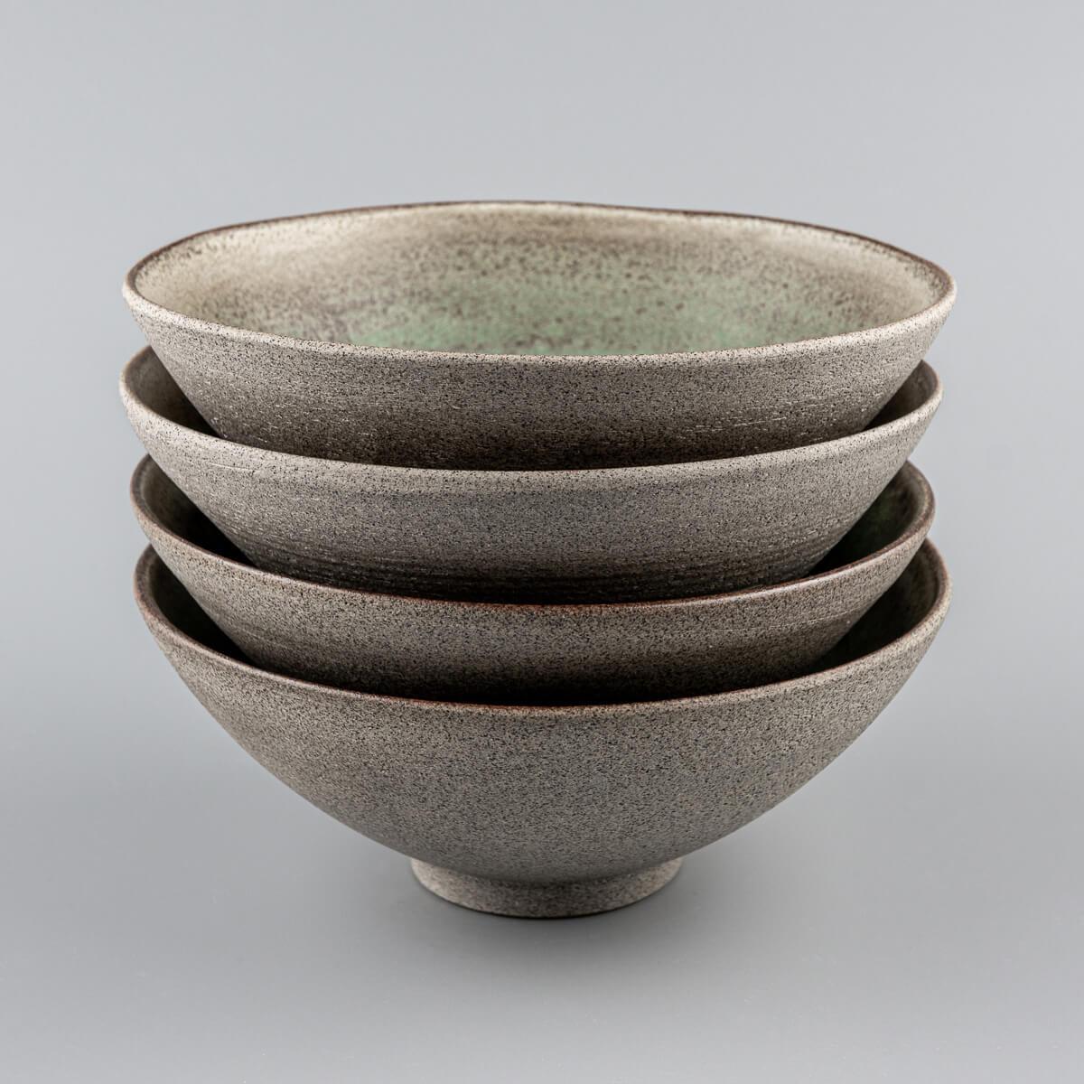 Stacked handmade ceramic bowls with green glazed interiors and unglazed stoneware exteriors.