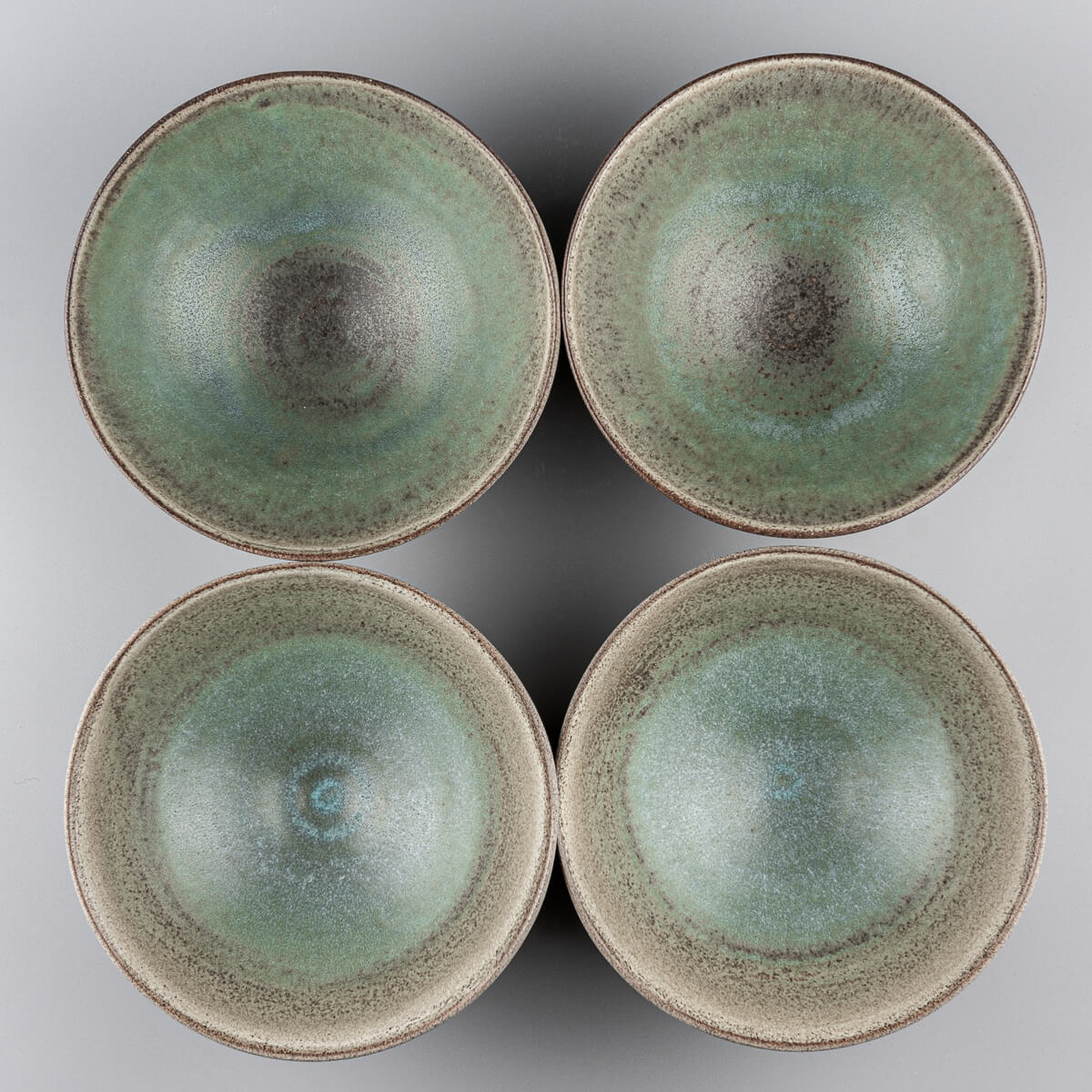 Top view of four handmade ceramic bowls with green interiors and textured clay finish.