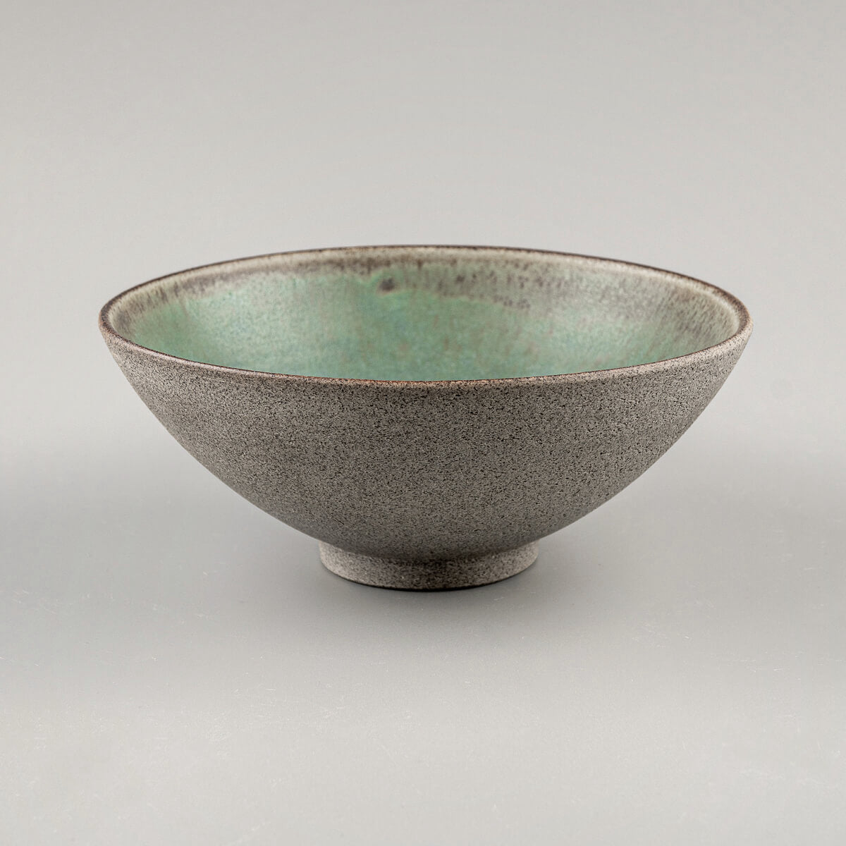 Side view of a handmade ceramic bowl with elevated foot and curved shape.