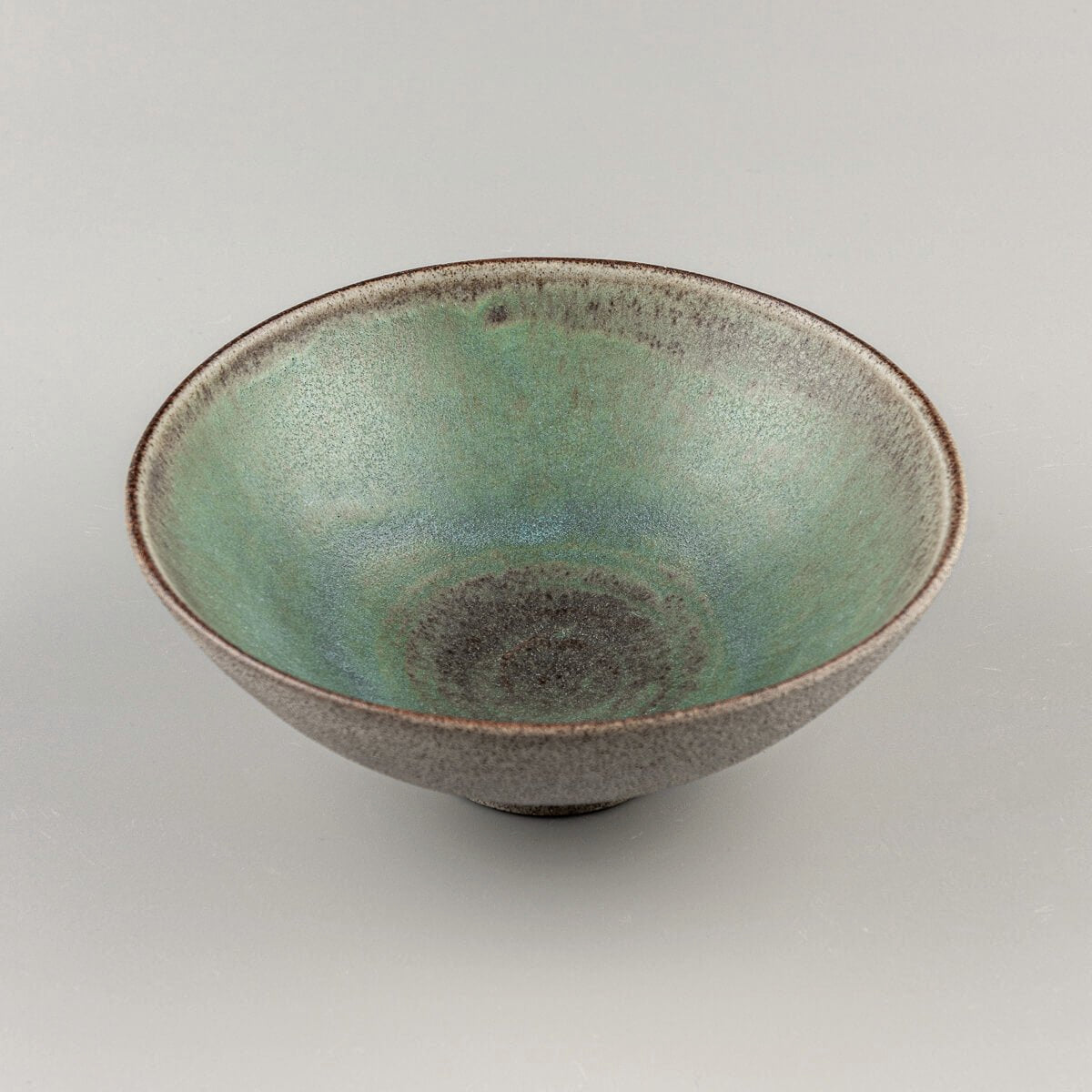 Isolated handmade bowl showing smooth green glaze and raw textured clay.