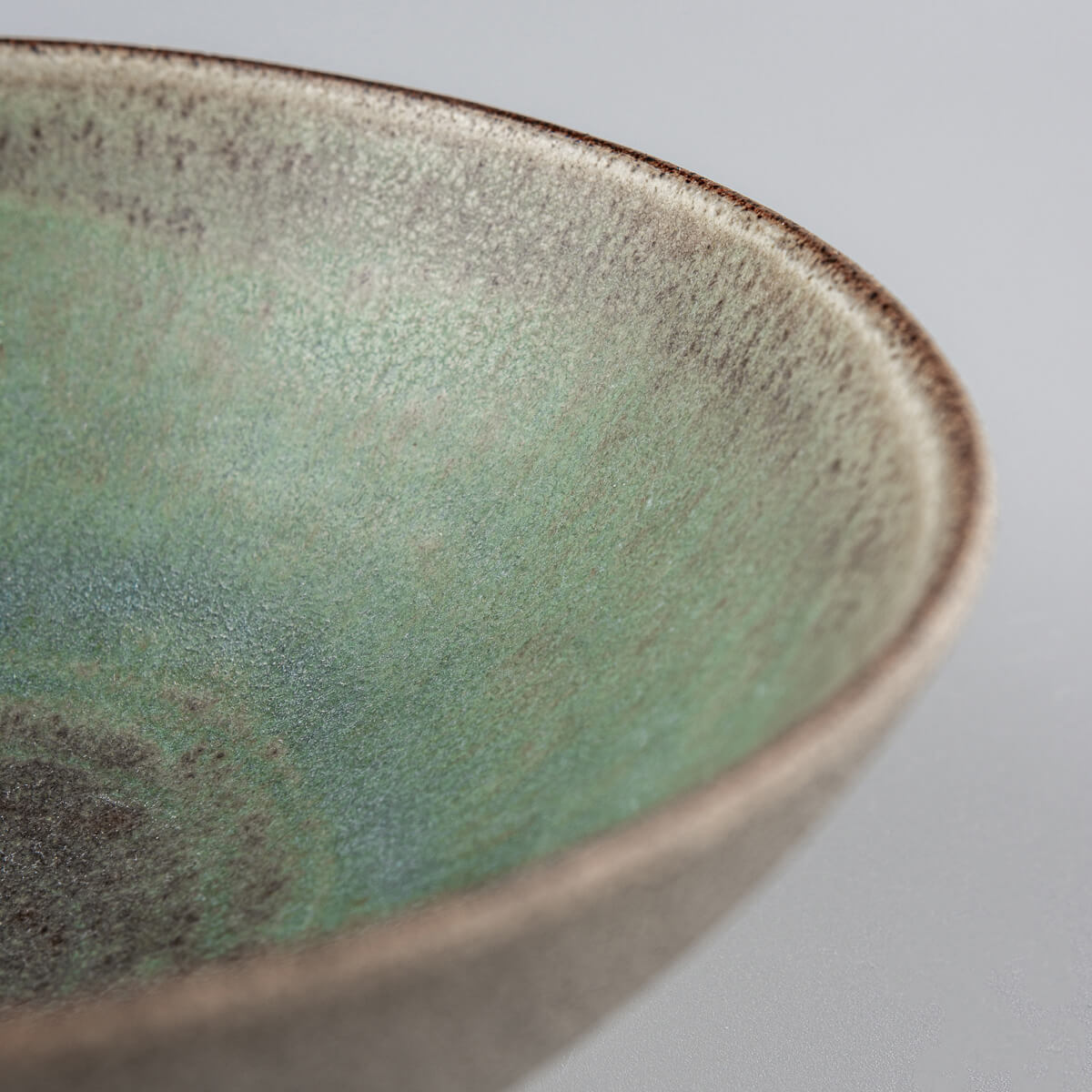 Detailed view of natural clay texture contrasting with soft green glaze in artisanal bowl.