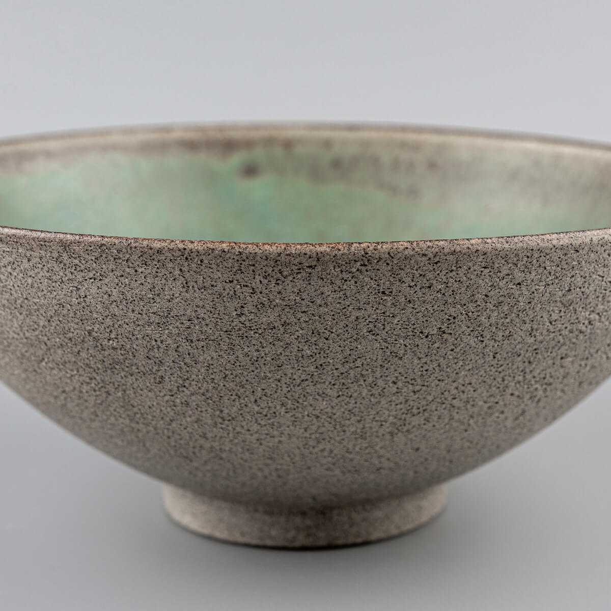 Handmade stoneware bowl with matte green glazed interior and unglazed textured dark clay exterior, ideal for restaurant.