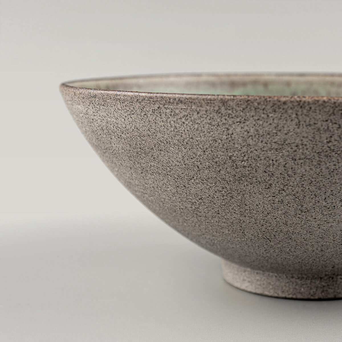 Profile of a ceramic bowl with elegant foot and rustic stoneware surface.