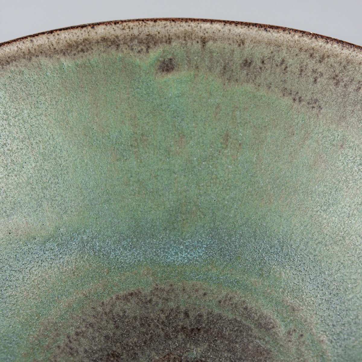 Green-glazed interior of a ceramic bowl with handcrafted texture and depth.